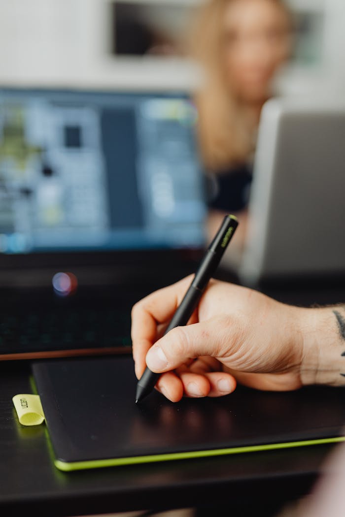 Focused shot of a persons hand using a stylus on a digital tablet, with a blurred background.
